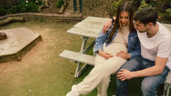 A photograph of a pregnant and a man sat together on a bench.