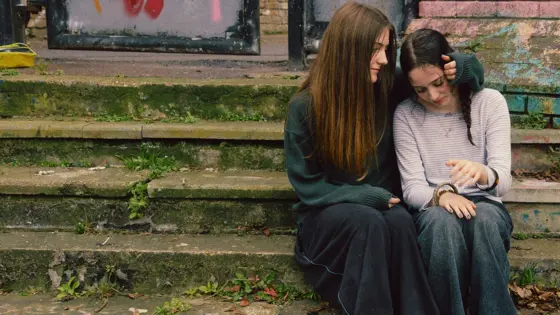 Two young girls sat on on steps, with one comforting the other.