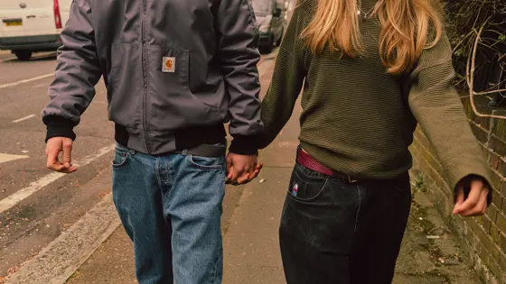 A young couple walking down the street holding hands with their faces not shown