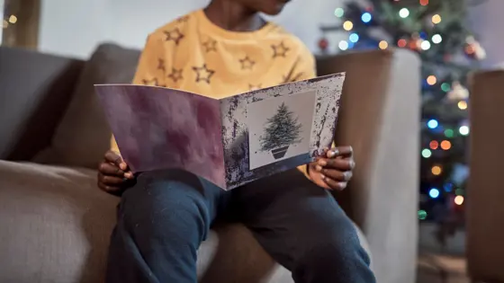 Child reading a card with a Christmas tree in the background.