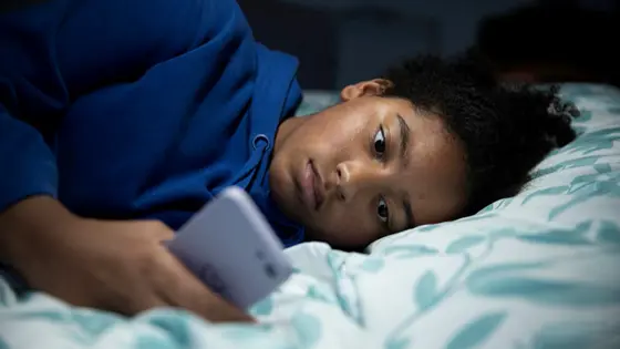 A young person lying in bed on their phone. The lights are off, they're meant to be asleep.