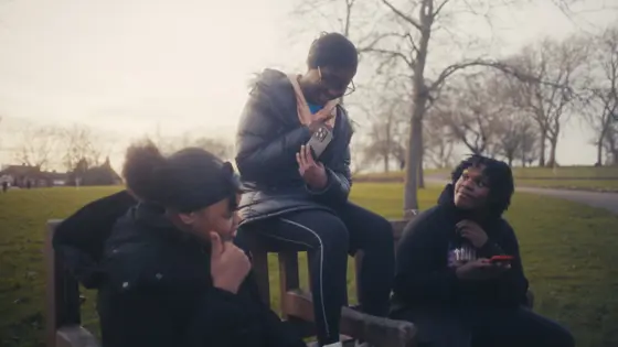 Three young adults sat on a bench, talking and taking photos.