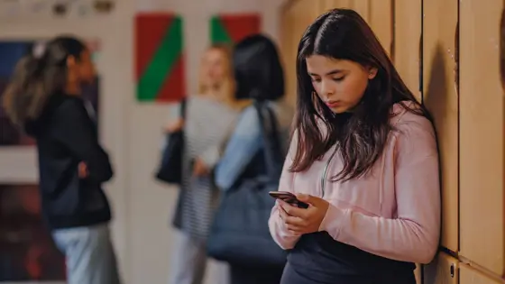 Photo of a teenager in school looking down at their phone.