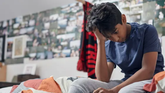 Boy sitting on their bed looking down.