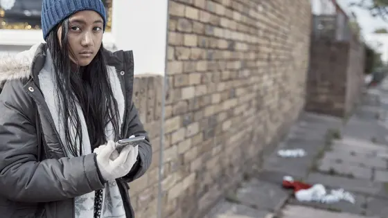 A young person stood outside by a wall using a mobile phone