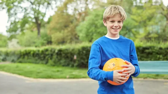A teenager smiling while holding a ball in a park.