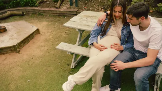A photograph of a pregnant and a man sat together on a bench.