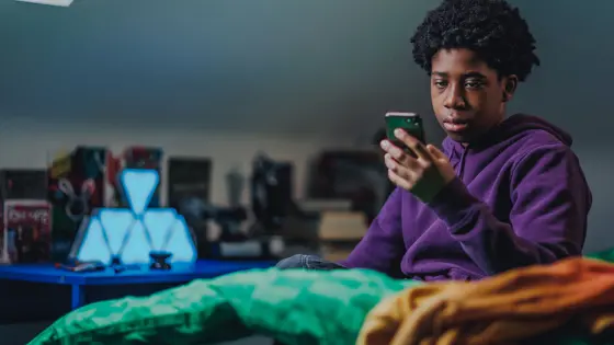 A young person looking at their phone in their bedroom and looking unhappy