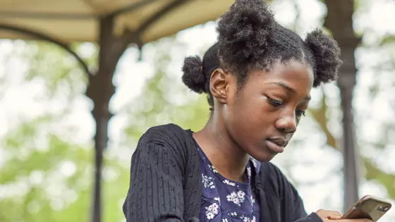 Photo of a young person standing outside looking down at their phone.