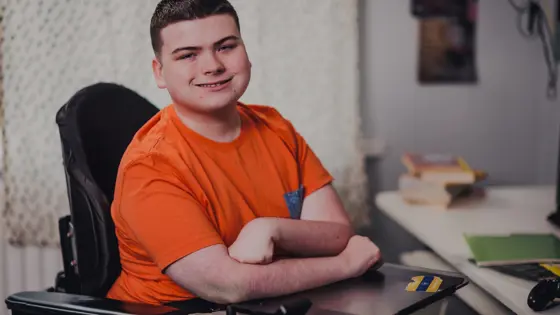 A young person in motorised wheelchair, they are looking at the camera and smiling.