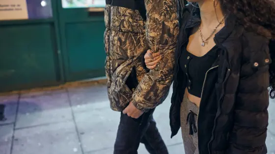 Photo of a teenage couple walking on the pavement in the evening.