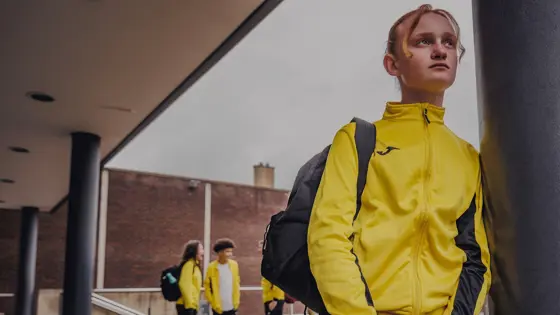 Photograph of a girl standing outside and wearing a yellow tracksuit.