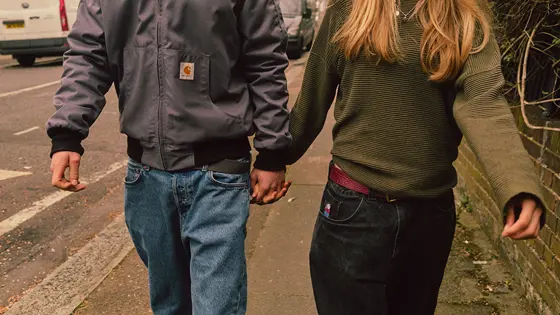 A young couple walking down the street holding hands with their faces not shown