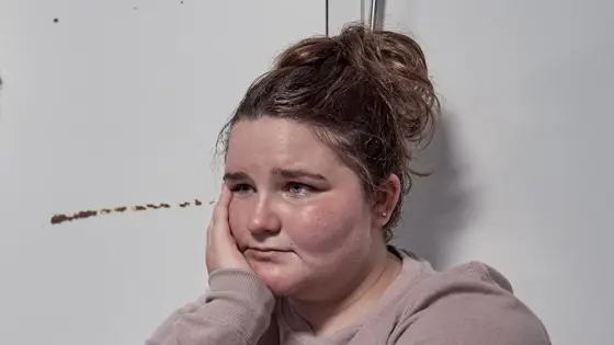 A young person sitting down with their head supported by their hand and looking sad