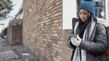A young person standing on the street and looking at their phone