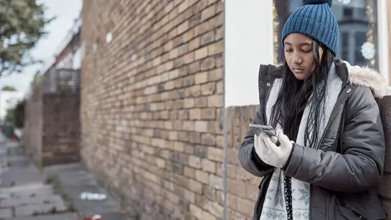 A young person standing on the street and looking at their phone