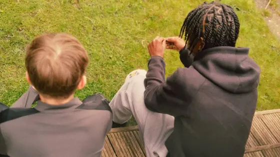 Photograph of two teenagers sat outside.