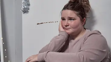 A young person sitting down with their head supported by their hand and looking sad