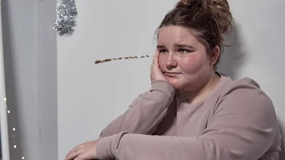 A young person sitting down with their head supported by their hand and looking sad