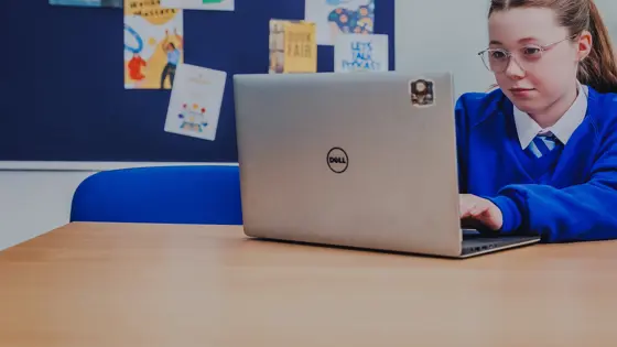 A young girl sat with a laptop in school