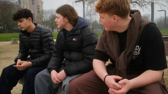 Photograph of three young people sat in a park.