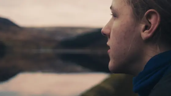 Photograph of a teenager outside, looking out at a lake.