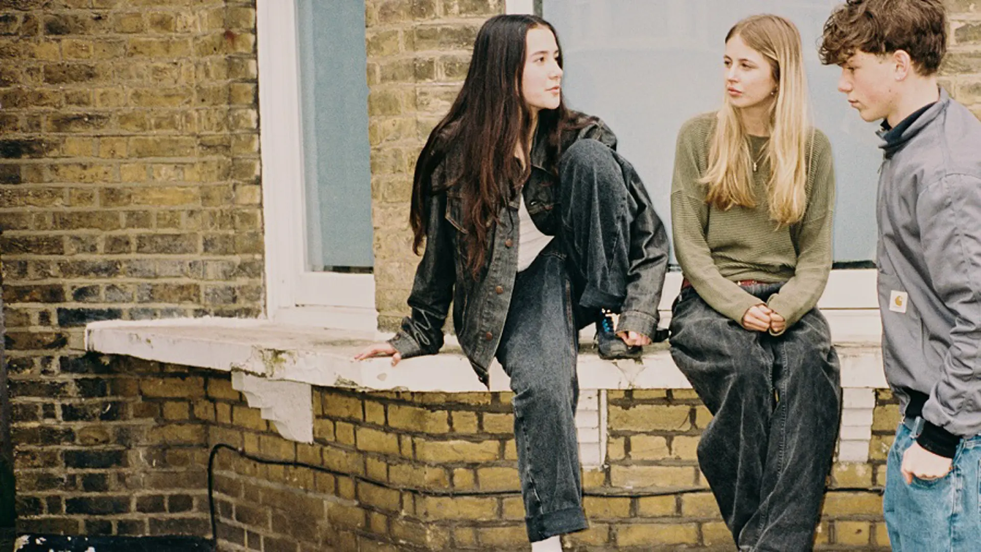 Two teenage girls and a teenage boy sat on a wall outside