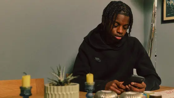 Photograph of a teenager using their mobile phone indoors.