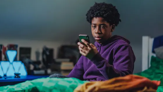 A young person looking at their phone in their bedroom and looking unhappy