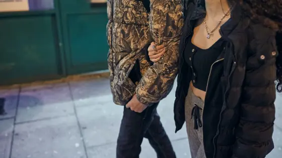 Photo of a couple walking down the street at night with their arms linked together.
