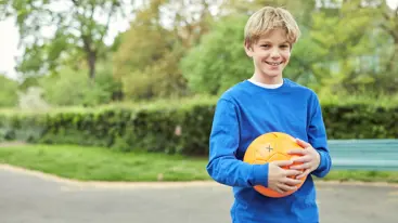 A teenager smiling while holding a ball in a park.