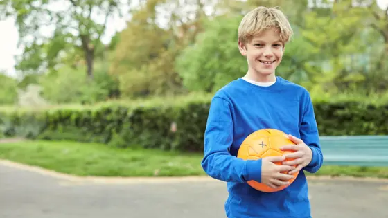 A teenager smiling while holding a ball in a park.