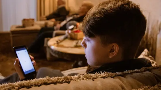 Photo of a teenager in a living room looking at their phone.