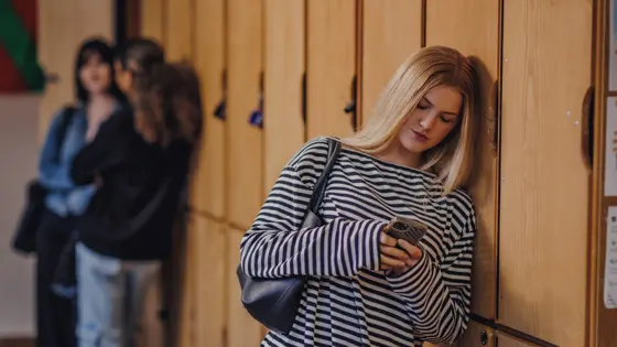 Photo of a teenager staring at their phone while leaning against a wall.