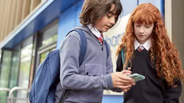 A young boy and young girl look at a phone together while outside.