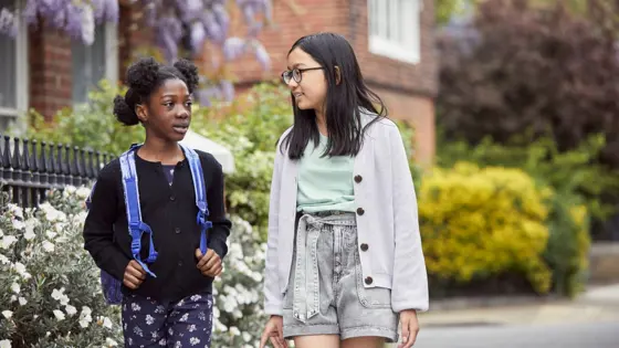 Photograph of two girls talking while walking down a street.