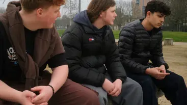 Photograph of three young people sat in a park.