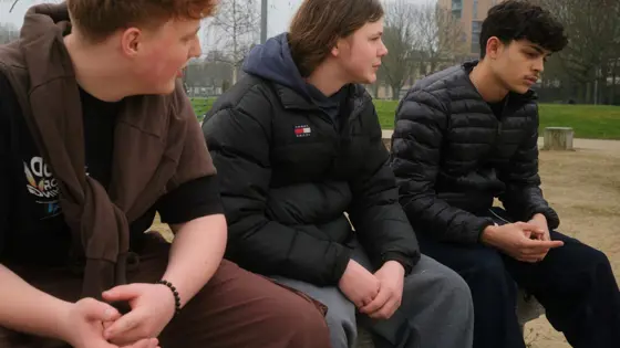 Photograph of three young people sat in a park.