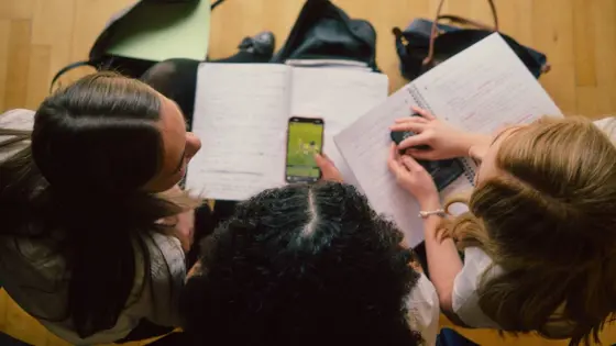 Photograph of three teenagers in school wih workbooks and mobile phones.