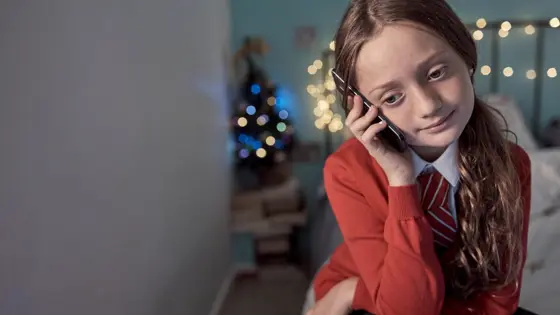 Photograph of a young person on the phone with Christmas decorations in the background.