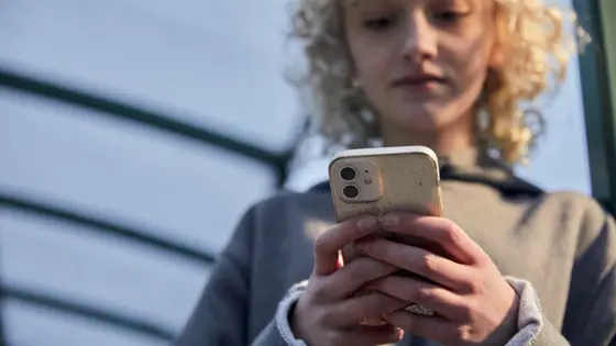 Photo of teenager standing outside looking at their phone.