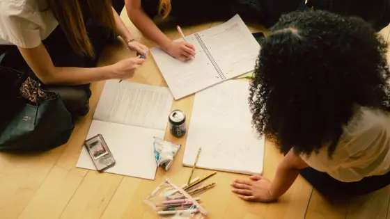 Photograph of four young people sit on a floor doing school work.