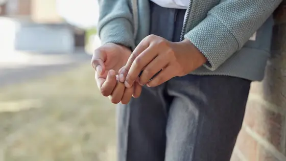 Close up photo of a young person's hands while they lean against a wall.