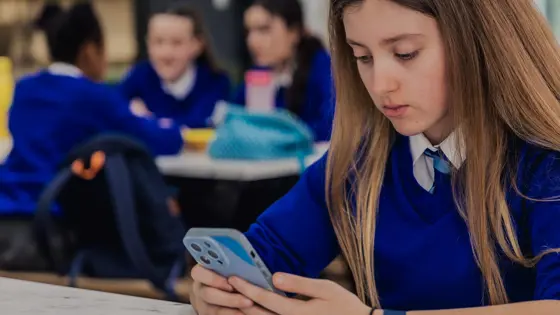 Photo of someone in a blue school uniform sitting at a table looking at their phone.