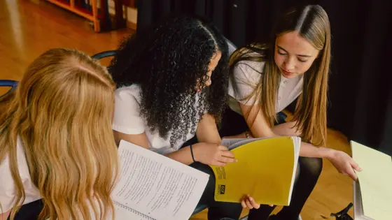 Photograph of three teenagers in school uniform, looking through their workbooks.