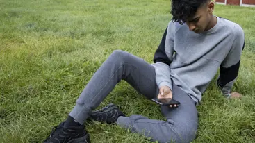 Teenage boy sat on the grass looking at his phone
