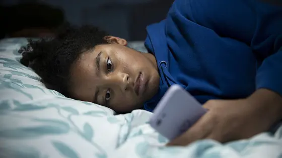 Teenage girl lay down in bed on mobile phone.