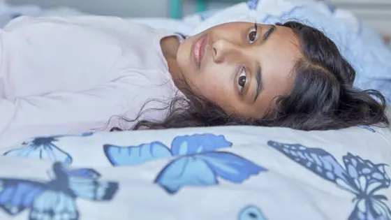 A young person lying on their bed during the day with their eyes open.