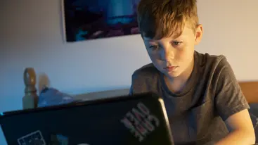 A young person using a laptop in their bedroom