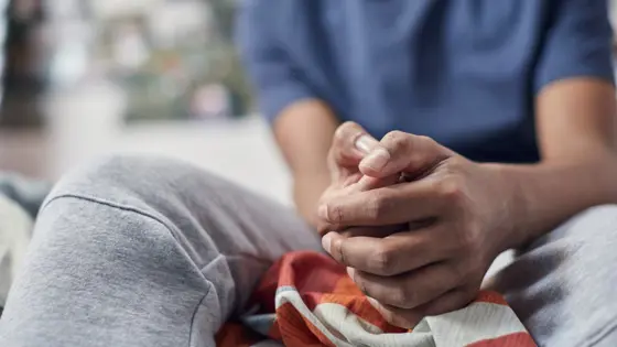 Close up photo of a teenager's hands clasped together while they sit on a bed.